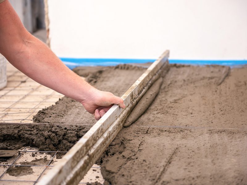 bricklayer aligns cement screed in a newly built house.